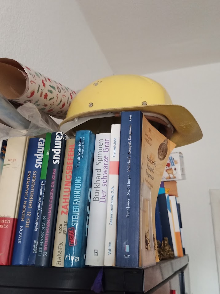 Foto zeigt Bauarbeiterhelm auf Büchern.
